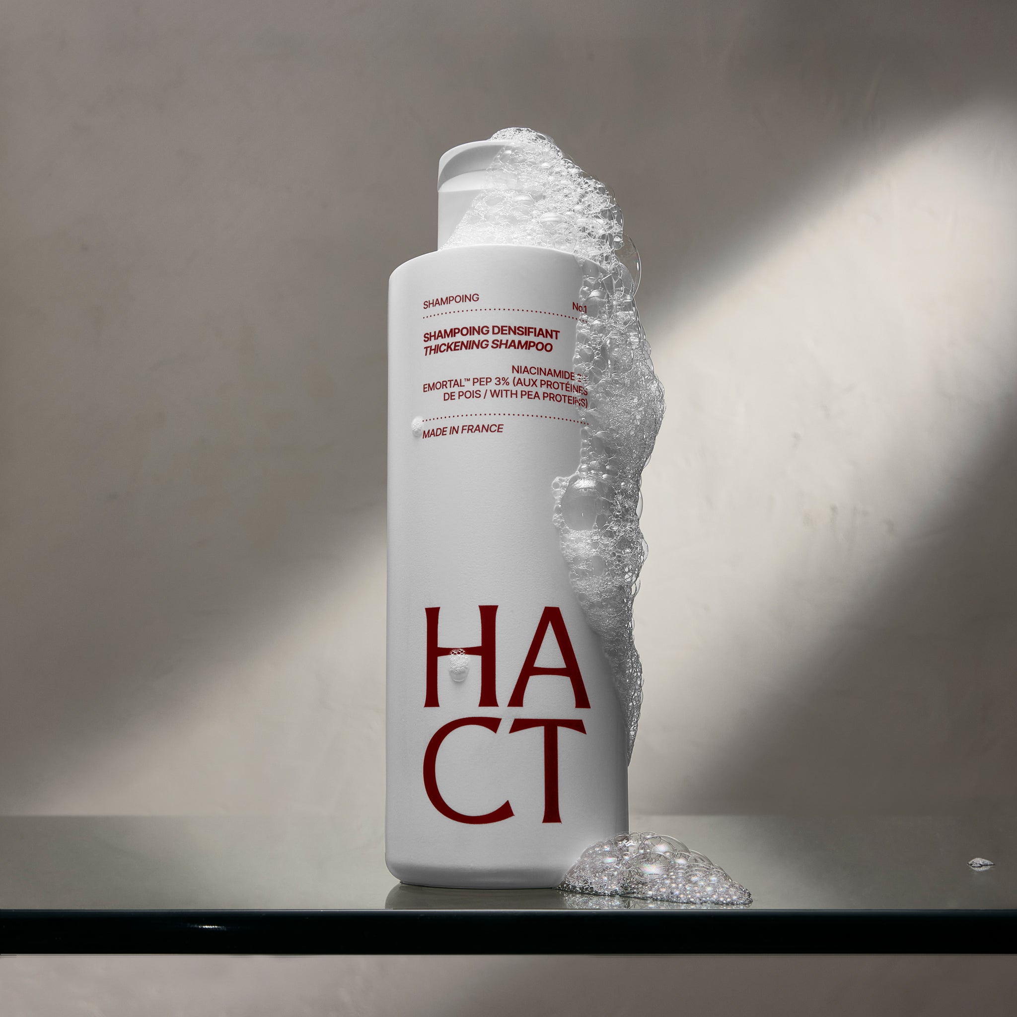 mousse qui dégouline sur un shampoing sur du verre