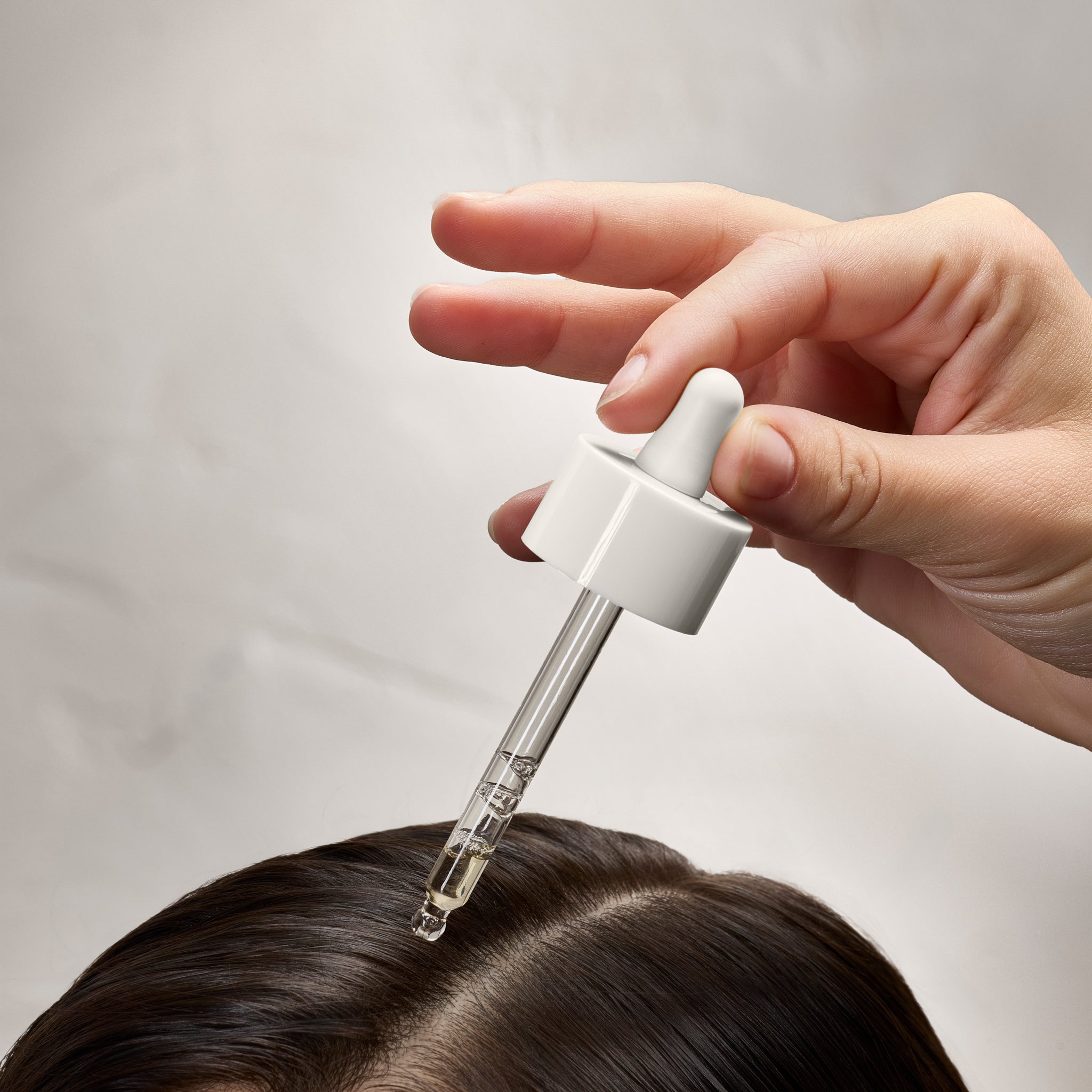 pipette tenue par une main au dessus d'une cuir chevelu